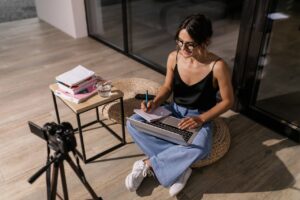 Woman in Black Tank Top Sitting on Ottoman Using Laptop